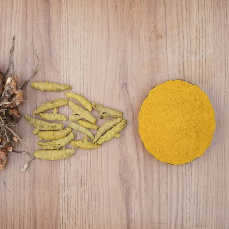 Fresh turmeric and ginger roots with black peppercorns on textured travertine stone.